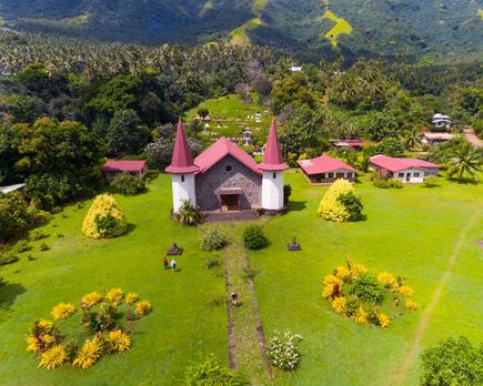 Luftaufnahme eines kleinen Dorfes mit Kirche auf Nuku-Hiva, Französisch-Polynesien, beliebtes Ausflugsziel für Aranui 5 Reisende