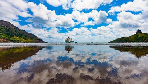 The ship Aranui 5 in front of a Southsea panorama of the Marquesas island Hiva Oa with ocean and green hills 