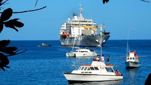 The ship Aranui 5 in front of a South Sea panorama of the Marquesas island Tahuata with ocean and clear blue sky