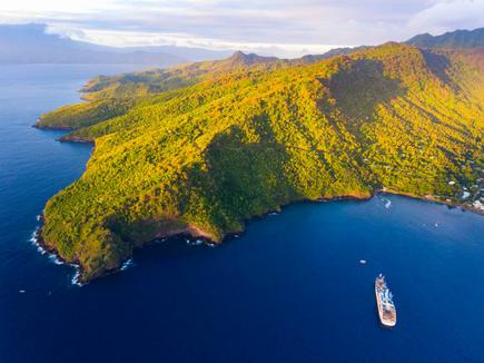 Aerial view of the sea with the Aranui 5 and the green hills of Tahuata, French Polynesia, with the ship Aranui 5 off the coast