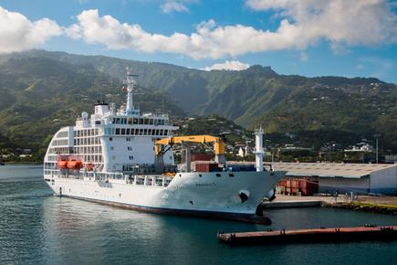 The mail ship Aranui 5 in front of a South Seas panorama of the Marquesas Island in French Polynesia with sea and green hills 