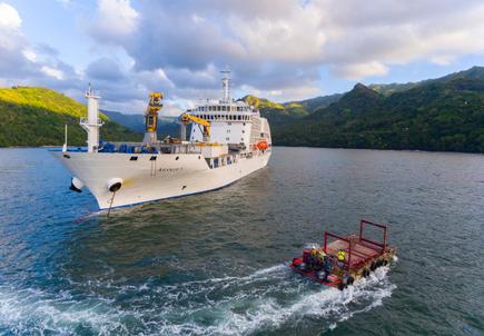 The mailboat Aranui 5 and pontoon in front of a South Sea panorama of the Marquesas Islands with blue sky and green hills 