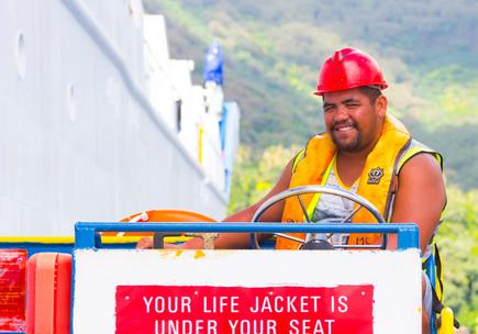Lächelnder Aranui 5 Cargo Arbeiter mit gelber Weste und rotem Helm auf Hebebühne