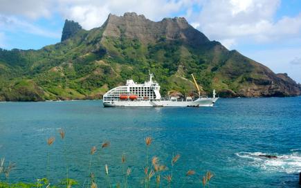 Das Postschiff Aranui 5 vor einem Südsee Panorama der Marquesas Inseln mit Meer und grünen Hügeln 